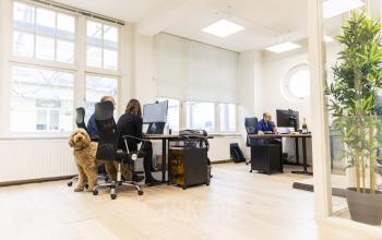 Lichte kantoorruimte op Prins Hendrikkade 21, Amsterdam Centrum met moderne werkplekken, grote ramen en mensen druk werkend achter computers. Geschikt voor bedrijven die kantoorruimte willen huren.