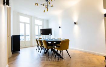 Stijlvolle, lichte conferentieruimte met elegante houten vloer, lange tafel, moderne stoelen en groot scherm. Gelegen aan de Prins Hendrikkade 21, Amsterdam Centrum. Ideaal voor kantoorruimte huren en professionele bijeenkomsten.