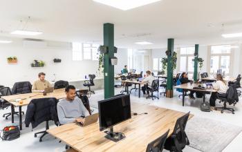 Ruime kantoorruimte huren aan de Prins Hendrikkade 21 in Amsterdam Centrum, met meerdere mensen hard aan het werk achter bureau's en laptop's, omringd door groene planten en natuurlijke lichtinval.