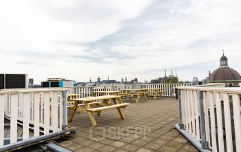 Dakterras met houten picknicktafels op Prins Hendrikkade 21, omgeven door het stadszicht van Amsterdam Centrum, ideaal voor kantooractiviteiten en verhuur.
