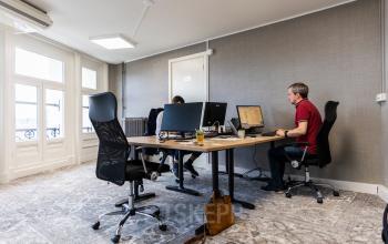 Modern kantoorpand aan de Prins Hendrikkade 21 in Amsterdam Centrum, met gemeubileerde werkplekken en personen die geconcentreerd aan computers werken. Perfecte locatie om kantoorruimte te huren.