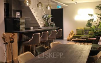 Stijlvolle binnenruimte met een moderne bar, gouden accenten en comfortabele zitplekken, ideaal voor een professionele omgeving in Amsterdam Centrum. Kantoorruimte huren met karakter.