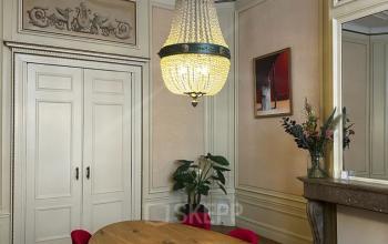 Elegante kantoorruimte in Amsterdam Centrum met een grote houten vergadertafel, rode stoelen en een indrukwekkende kroonluchter. Perfect voor formele bijeenkomsten en vergaderingen.