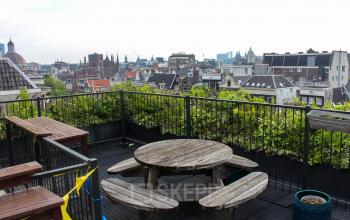 Dakterras met houten tafel en bankjes op Singel 126 in Amsterdam Centrum, ideaal voor kantoorgebruik, biedt een prachtig uitzicht over de stadssilhouetten.