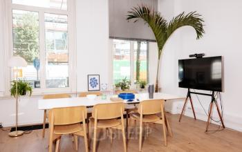 Moderne kantoorruimte huren in Amsterdam Centrum, met houten tafel, stoelen, grote ramen en decoratieve planten. Voorzien van een tv voor presentaties. Ideaal voor vergaderingen en vergaderruimtes.