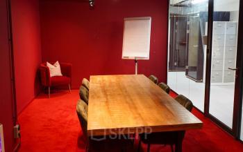 Vergaderruimte met houten tafel en stoelen in kantoorpand op Weesperplein 4b, Amsterdam Centrum. De ruimte heeft rode muren en vloerbedekking en is ideaal voor kantoorruimte huren.