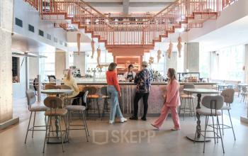 Open en moderne kantoorruimte op Weesperplein 4b, Amsterdam Centrum met stijlvolle bar en mensen in gesprek. Ideaal voor vergaderingen en creatieve werkplekken. Uitstekende faciliteiten voor kantoorruimte huren.