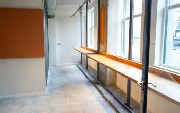 Lichte kantoorruimte te huur op Weesperplein 4b, Amsterdam Centrum met grote ramen en houten werkblad langs de muur, ideaal voor werkomgeving.
