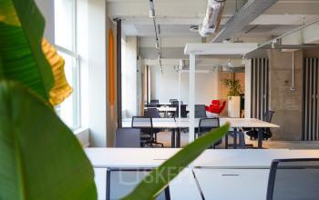 Kantoorruimte huren op Weesperplein 4b, Amsterdam Centrum, met moderne werkplekken, een rode fauteuil en veel daglicht.
