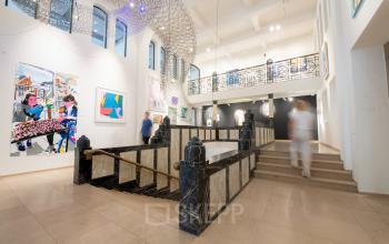 Binnenruimte van een kantoorpand op Weesperplein 4b in Amsterdam Centrum met moderne kunstwerken en open trap. Personen bewegen door de ruimte, wat de dynamiek van de werkplek benadrukt.