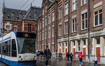 Kantoorpand aan Stationsplein 9 in Amsterdam Centrum, naast een tramhalte, met mensen die langs de straat lopen. Mogelijkheden om kantoorruimte te huren.