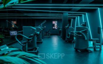 Moderne fitnessruimte met verschillende trainingsapparaten, gelegen in het kantoorpand op Stationsplein 9, Amsterdam Centrum. Ruimte heeft opvallende blauwe LED-verlichting.