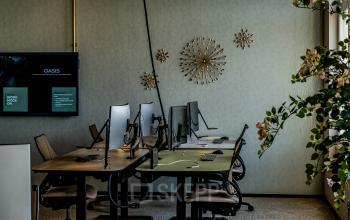 Moderne kantoorruimte huren op Stationsplein 9, Amsterdam Centrum, met meerdere werkplekken, bureaus en beeldschermen. Decoratieve wandelementen en groene planten zorgen voor een inspirerende werkomgeving.