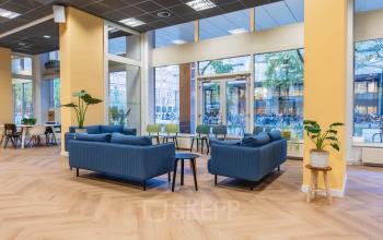 Lichte en moderne kantoorruimte met grote ramen en blauwe banken op de Weesperstraat 107-121. Deze kantoorruimte in Amsterdam Centrum biedt comfortabele zitgedeeltes en uitzicht op de straat.