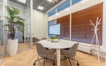 Kantoorruimte huren in Amsterdam Centrum: een lichte vergaderruimte met moderne inrichting, glazen wanden en een groot scherm op Weesperstraat 107-121. Ideaal voor productieve bijeenkomsten in een kantoorpand.