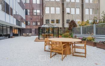 Buitenruimte van het kantoorpand aan de Weesperstraat 107-121, Amsterdam Centrum, met houten tafels en plantenbakken, ideaal voor een pauze of informele vergadering. Geschikt voor bedrijven die kantoorruimte willen huren.