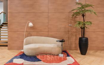 Moderne kantoorruimte op Weesperstraat 107-121 in Amsterdam Centrum met houten panelen, een design bank, vloerlamp, kleurrijk tapijt en een grote plant. Prima plek voor kantoorruimte huren.