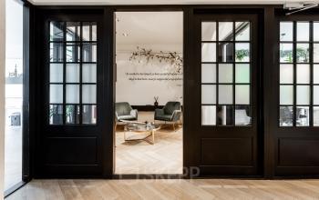 Stijlvolle lounge op Rokin 46-1 in Amsterdam Centrum met houten vloer, moderne fauteuils en glazen deuren. Perfect voor kantoorruimte huren met een ontspannen sfeer.