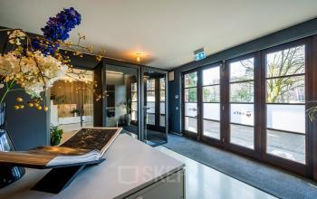 Ingang van het kantoorpand op Groenmarktkade 5-H, Amsterdam Centrum met glazen deuren en decoratieve bloemen, ideaal voor kantoorruimte huren.