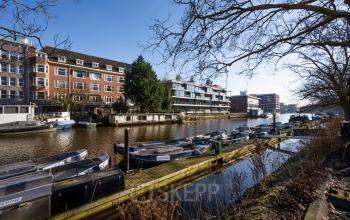 Kantoorpand gelegen aan de Groenmarktkade 5-H, Amsterdam Centrum, met aangrenzend een gracht en aangemeerde boten, ideaal voor inspirerende zakelijke besprekingen. Perfecte locatie voor kantoorruimte huren in een dynamische stad.