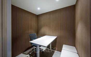 Modern kantoorpand in Amsterdam Centrum met strak interieur, houten wanddecoratie en een bureaustoel naast een lange tafel. Ideaal voor kantoorruimte huren in een stijlvolle omgeving.