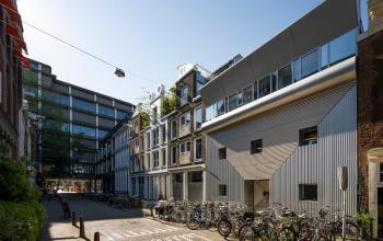 Kantoorpand in Amsterdam Centrum op Kerkstraat 204, omringd door fietsen. Moderne architectuur en een lichtblauwe lucht benadrukken de stedelijke sfeer. Ideale locatie om kantoorruimte te huren.