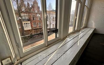 Uitzicht vanaf een grote vensterbank in een kantoorpand aan de Nieuwezijds Voorburgwal 340, Amsterdam Centrum. De kamer is ongemeubileerd en rustig, ideaal om kantoorruimte te huren met karakteristieke ramen.