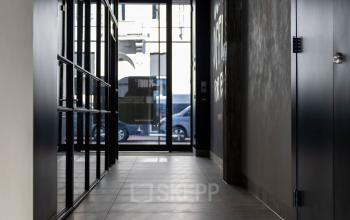 Gang in een kantoorpand aan de Pieter Cornelisz. Hooftstraat 7 in Amsterdam Centrum, met zicht op glazen deuren. De ruimte oogt strak en modern.