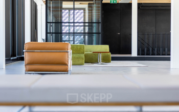 Heldere kantoorruimte met moderne meubels en veel natuurlijk licht, ideaal voor wie een kantoorpand wil huren in Amsterdam Centrum. Houten balken zorgen voor een warme sfeer.