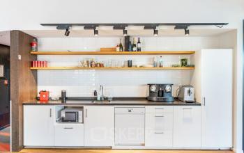 Gezellige pantry in een kantoorpand op Stadhouderskade 55, Amsterdam Centrum. Voorzien van moderne apparatuur en open schappen. Ideaal voor wie kantoorruimte wil huren.