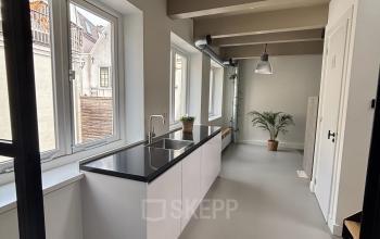 Lichte kantoorruimte te huur aan de Kloveniersburgwal 131K in Amsterdam Centrum, met moderne keuken en grote ramen. Het interieur is strak en uitnodigend.