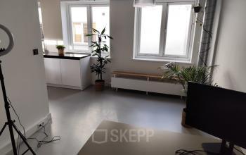 Lichte kantoorruimte in Amsterdam Centrum met moderne inrichting, geschikt om te huren. Het kantoorpand heeft grote ramen en is voorzien van planten en een bureau met scherm.