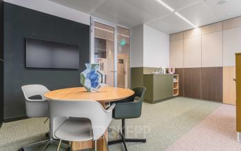 Kantoorruimte huren in modern kantoorpand aan de Piet Heinkade 55, Amsterdam Centrum. Stijlvolle vergadertafel met stoelen, geschikt voor zakelijke bijeenkomsten. Neutrale kleuren en glazen deuren creëren een lichte en open sfeer.