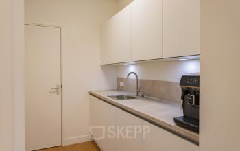 Moderne pantry in kantoorpand op Korte Leidsedwarsstraat 133A, Amsterdam Centrum, met witte kasten en espressomachine, ideaal voor huur in deze kantoorruimte.