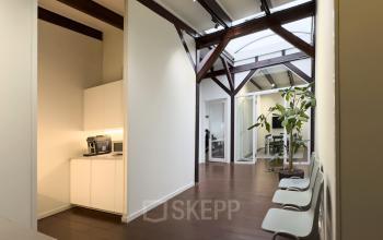 Moderne kantoorruimte te huur op Warmoesstraat 149 - 151, Amsterdam Centrum, met glazen wanden, houten vloeren en een gedeelde pantry. Planten en stoelen accentueren de inrichting van dit professionele kantoorpand.