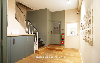 Ingang van een kantoorpand aan de Warmoesstraat 155 in Amsterdam Centrum met houten vloer en een trap naar boven. Kantoorruimte huren op een centrale locatie.