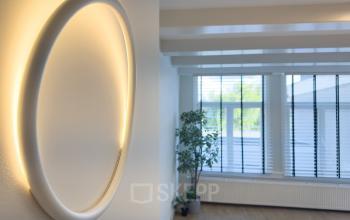 Kantoorruimte huren aan de Warmoesstraat 155 in Amsterdam Centrum met veel lichtinval, houten vloer en een moderne wandlamp. Planten zorgen voor een frisse uitstraling.