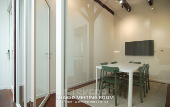 Gezellige vergaderruimte op Warmoesstraat 155, Amsterdam Centrum, ideaal voor kantoorruimte huren met moderne stoelen en een grote tafel, geschikt voor zakelijke besprekingen. Kantoorpand met houten vloer en tv-scherm.