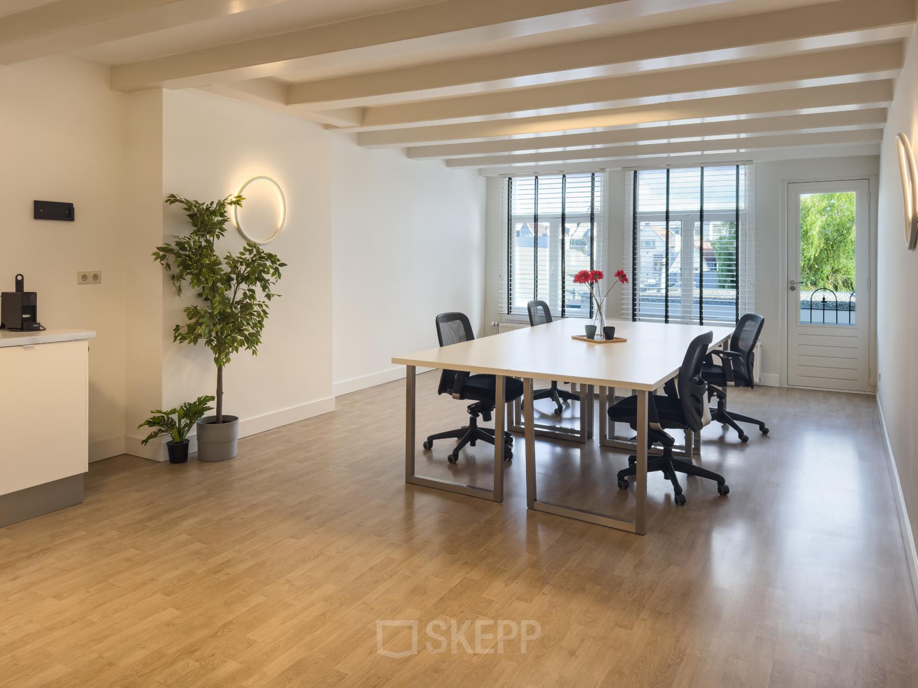 Ruime kantoorruimte huren aan Warmoesstraat 155 in Amsterdam Centrum met grote ramen, houten vloer en moderne bureaus. De zonnige werkplek is ingericht met comfortabele stoelen en groene accenten, ideaal voor productiviteit.