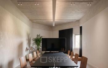 Stijlvolle vergaderruimte met houten stoelen rond een grote zwarte tafel, op Weteringschans 26 in Amsterdam Centrum. Ideale kantoorruimte voor bijeenkomsten of presentaties. Kantoorruimte huren beschikbaar.