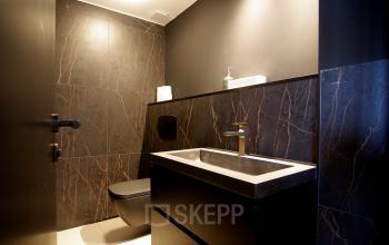 Moderne toiletruimte in een kantoorpand aan Kleine Gartmanplantsoen 21, Amsterdam Centrum, met donkere wandbekleding en een modern wastafelmeubel.