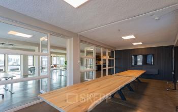 Moderne kantoorruimte te huur op Kleine Gartmanplantsoen 21, Amsterdam Centrum, met houten tafels en glazen wanden. Deze kantoorpand biedt een slimme werkruimte in het bruisende hart van de stad.