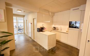 Moderne kitchenette in kantoorpand op Kleine Gartmanplantsoen 21, Amsterdam Centrum, met strakke witte kasten en apparatuur tegen een betonnen vloer en plafond. Kantoorruimte huren in een levendig gedeelte van Amsterdam.