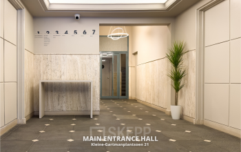 Ingang van een kantoorpand op Kleine Gartmanplantsoen 21 in Amsterdam Centrum. De ruimte heeft een strakke afwerking met een geometrisch patroon op de vloer, directe verlichting en af en toe een groene plant.