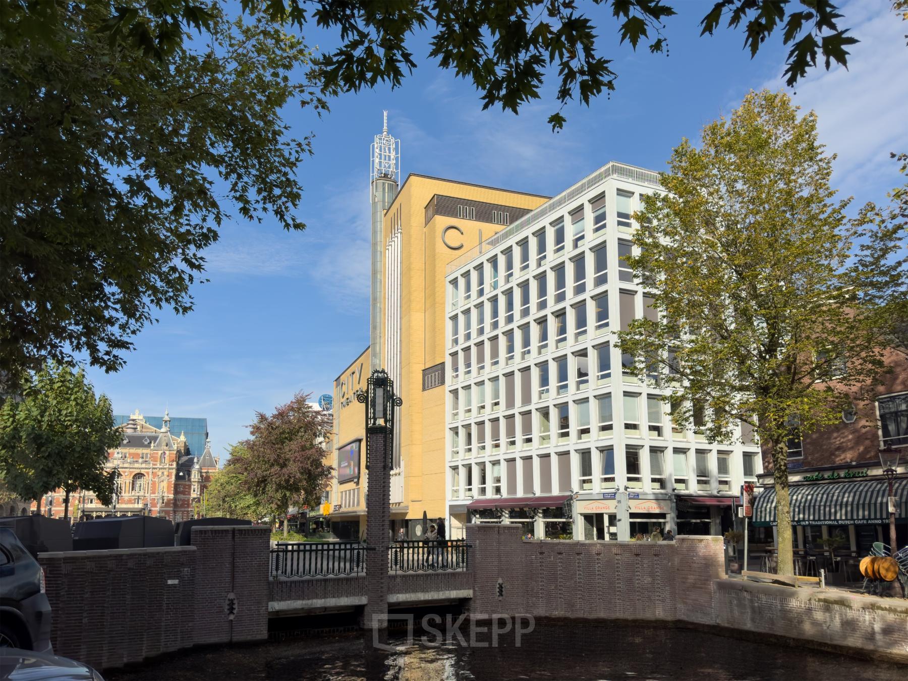 Kantoorpand aan Kleine Gartmanplantsoen 21 in Amsterdam Centrum met moderne gevel en omringd door bomen en water.