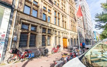 Straatbeeld van het kantoorpand aan de Nieuwezijds Voorburgwal 104-108 in Amsterdam Centrum, met meerdere fietsen geparkeerd voor het gebouw.