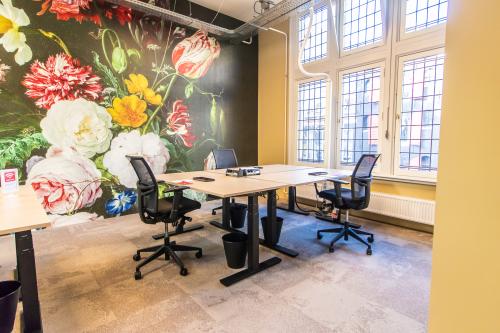 Lichte kantoorruimte te huur op Nieuwezijds Voorburgwal 104-108 in Amsterdam Centrum, met kleurrijke bloemenmuur, bureaus en stoelen. Grote ramen bieden veel daglicht.