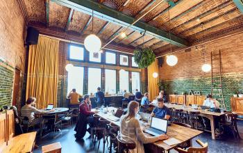 Gezellige kantoorruimte in Amsterdam Centrum, Oudebrugsteeg 9, met bakstenen muren, grote ramen en mensen geconcentreerd aan het werk.