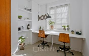Lichte kantoorruimte aan Vrijheidslaan 80, Amsterdam De Pijp, met een lang bureau, twee stoelen, planten en wandplanken. Ideaal om te huren voor rustige werkzaamheden in een inspirerende omgeving.