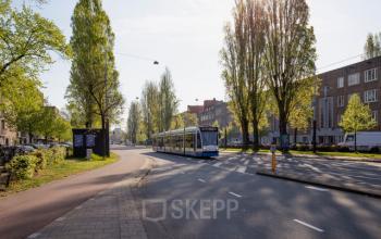 Exterieur van het kantoorpand op Vrijheidslaan 80 in Amsterdam De Pijp met groene omgeving en voorbijrijdende tram.